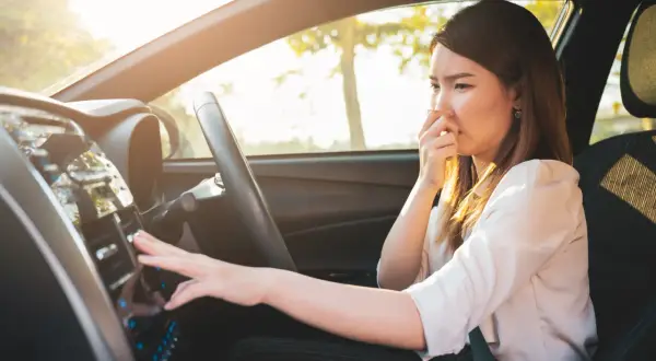 Frau hält sich die Nase zu, weil das Auto verbrannt riecht. Sie versucht, die Lüftung zu bedienen.