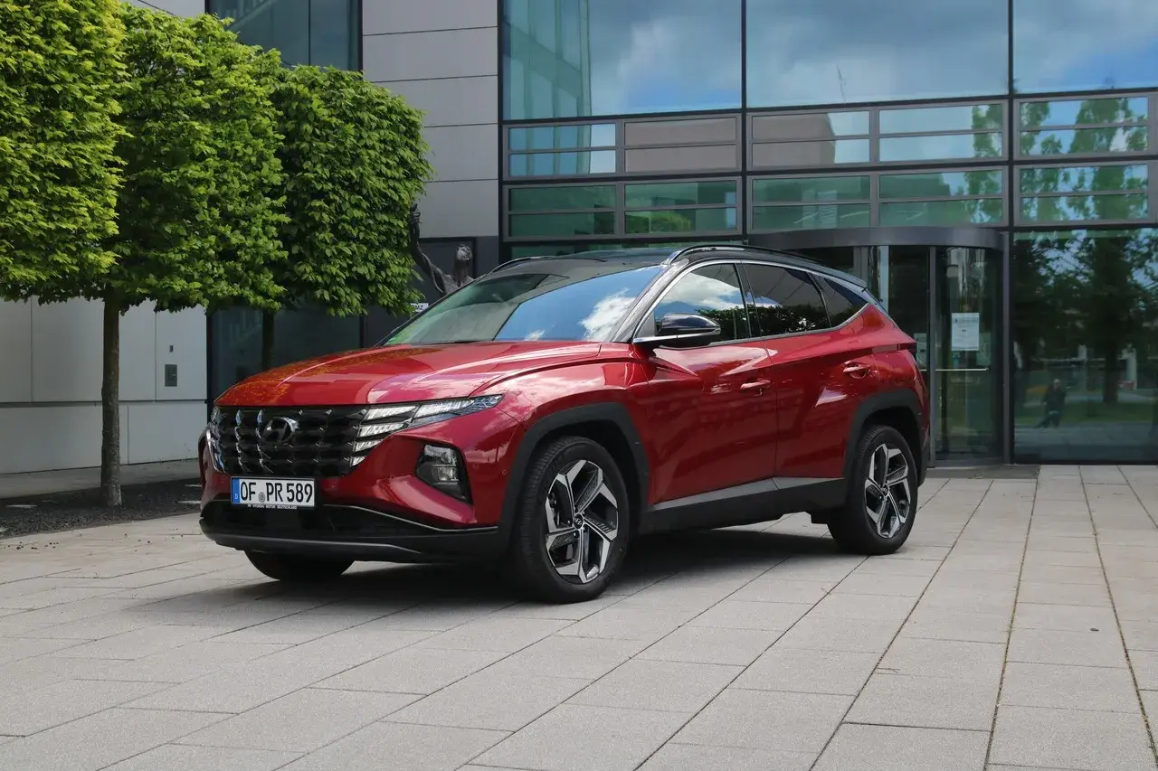 Roter Hyundai Tucson 2026 vor einem modernen Gebäude mit Bäumen.