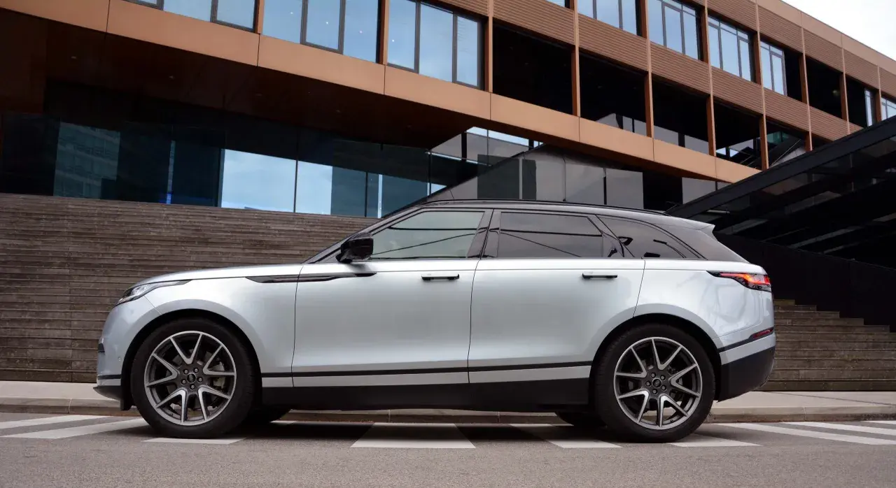 Silberner Range Rover Velar parkt vor moderner Architektur. Die eleganten Range Rover Velar Maße passen perfekt in das urbane Umfeld.