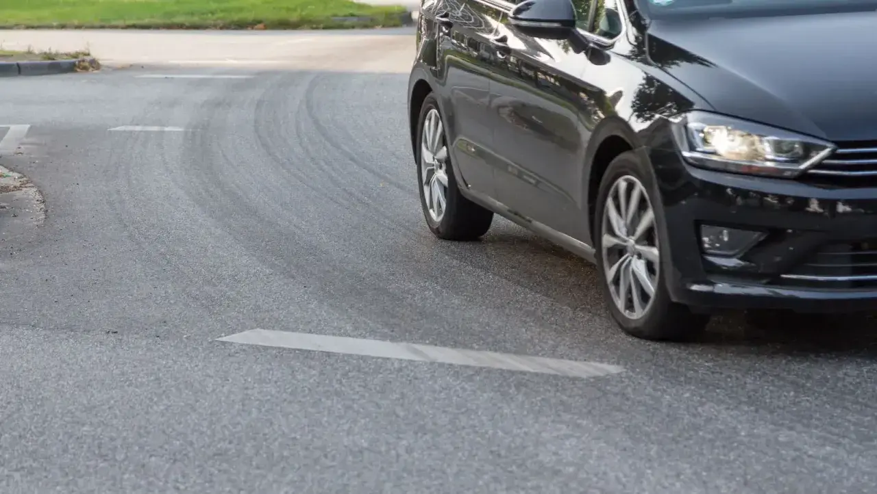 Schwarzes Auto fährt um eine Kurve, Reifen quietschen.