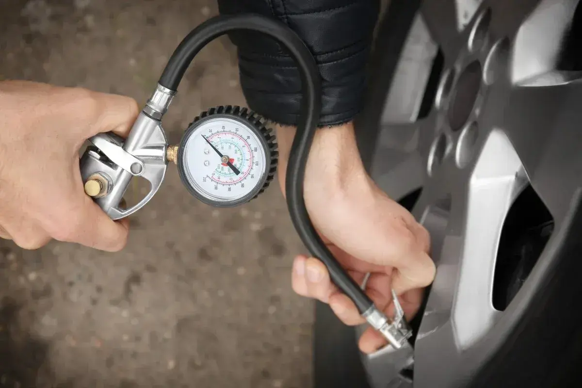 Person korrigiert den Reifendruck mit einem Manometer.