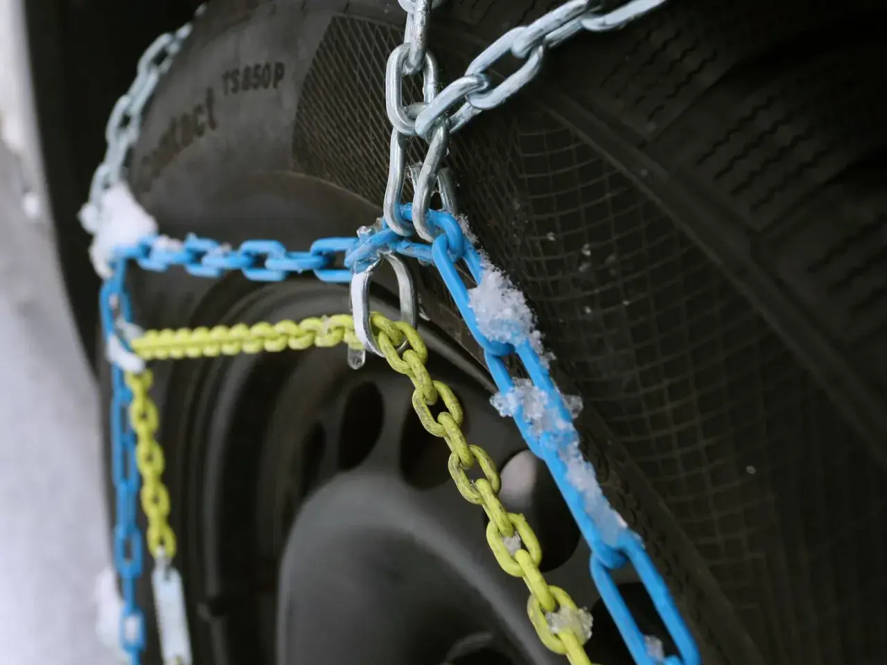 Schneeketten in Blau und Gelb sind an einem Reifen montiert, bereit für den Einsatz bei Schnee und Eis. Allradfahrzeuge profitieren besonders von dieser Traktionshilfe.