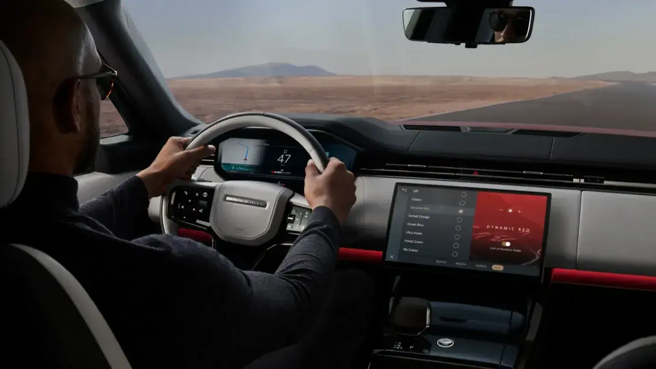 Mann fährt Range Rover, steuert über das intuitive Land Rover InControl System. Die Ambientebeleuchtung "Dynamic Red" leuchtet.