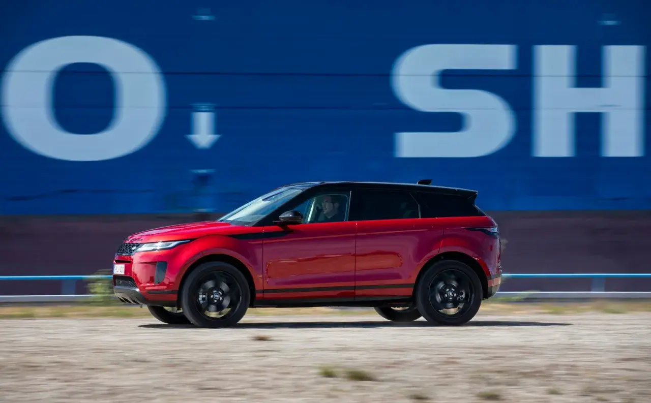 Roter Range Rover Evoque 2022 fährt an blauer Wand mit weißen Buchstaben vorbei.