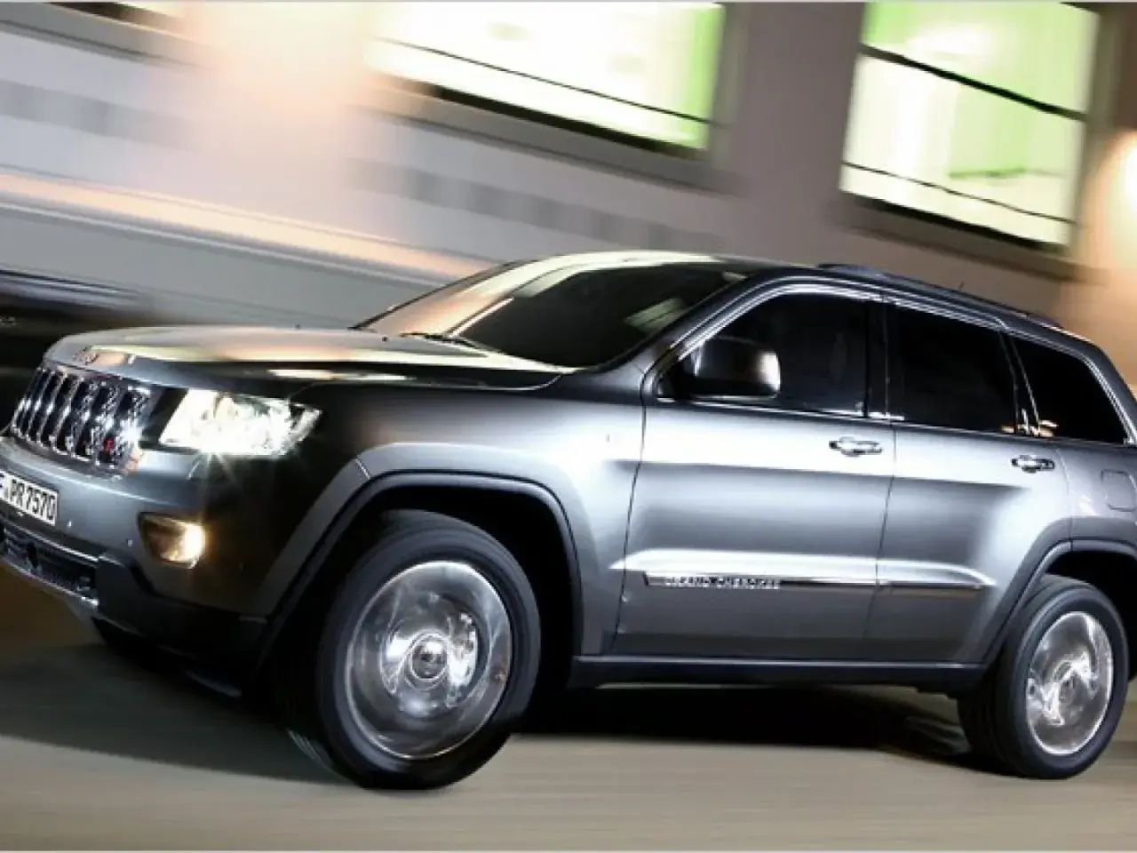 Grauer Jeep Grand Cherokee 3.0 CRD 250 PS in Bewegung, der auf der Straße fährt. Mögliche Probleme mit dem Motor sind hier nicht sichtbar.