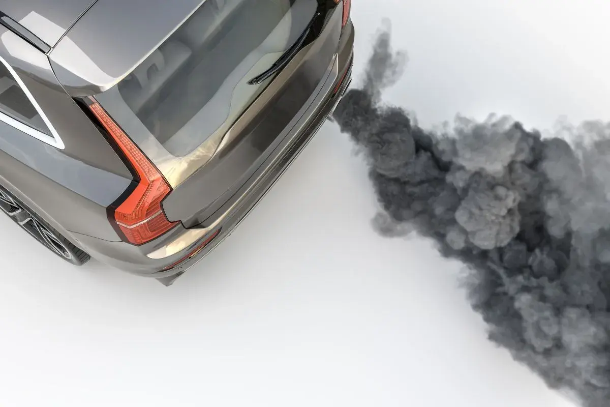 Graues Auto stößt dichten, schwarzen Rauch aus dem Auspuff aus.