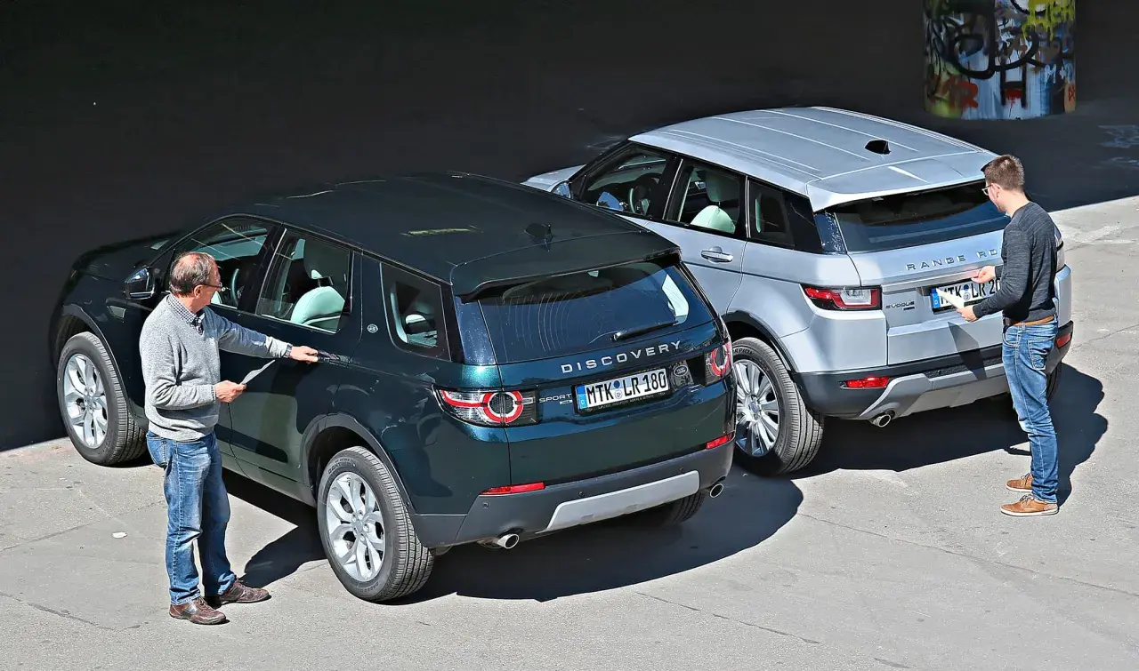 Zwei Männer inspizieren zwei Land Rover: einen dunklen Discovery Sport und einen silbernen Range Rover Evoque. Ein kleiner Land Rover, der Discovery Sport, steht im Vordergrund.