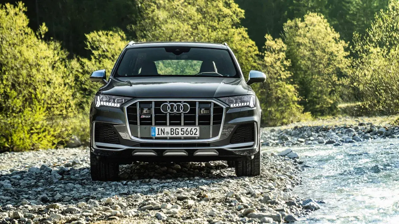 Ein dunkler Audi SQ8 PS steht am Ufer eines steinigen Flusses, umgeben von üppigem Grün.