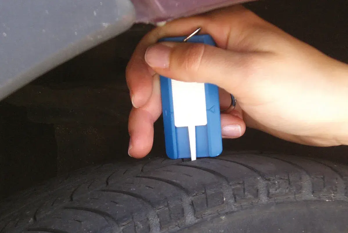 Hand misst Profiltiefe eines Reifens mit einem Messgerät. So prüfen Sie, wie alt Winterreifen sind.