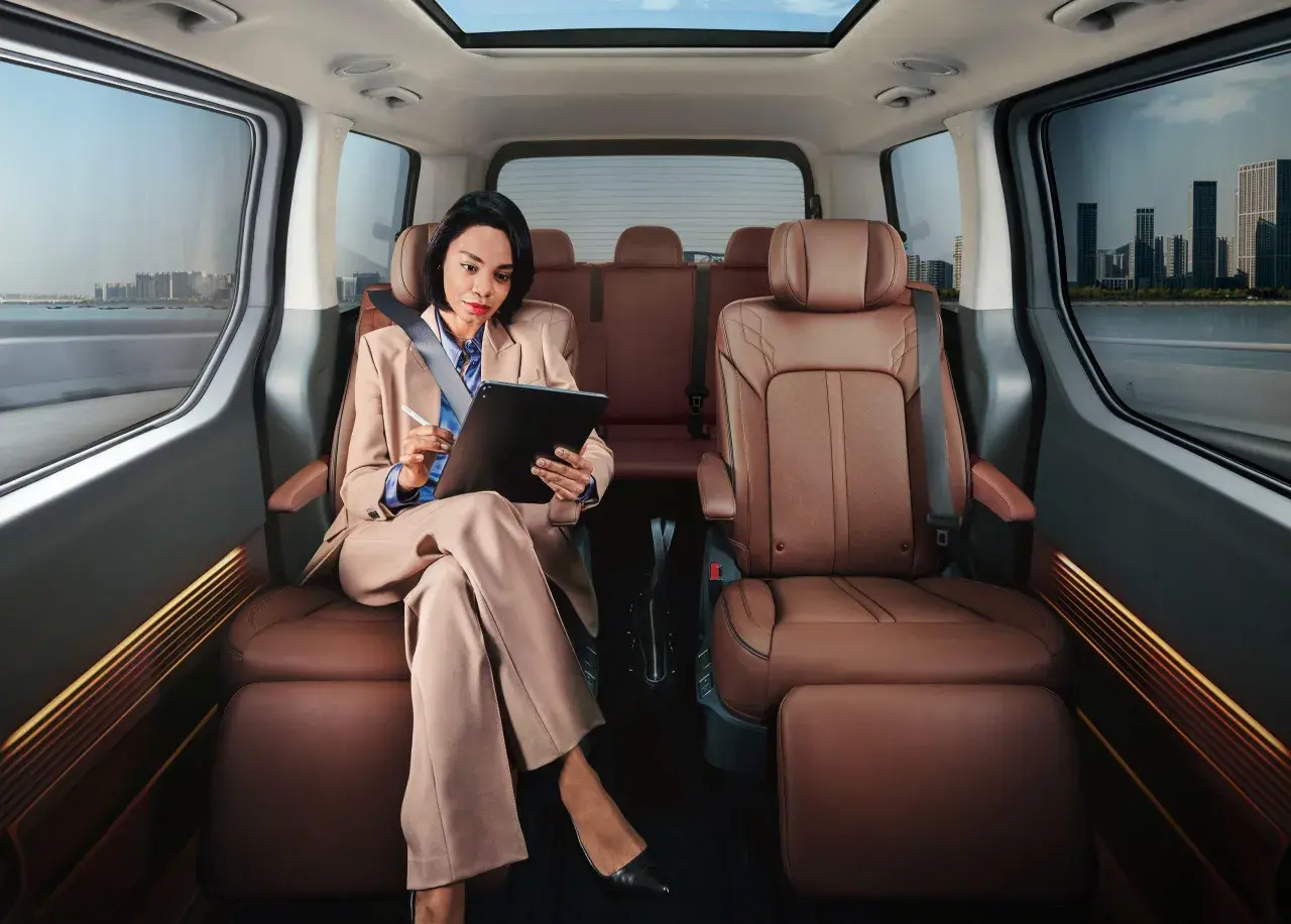 Frau arbeitet im luxuriösen Hyundai Staria Innenraum, während sie durch eine Stadt fährt.