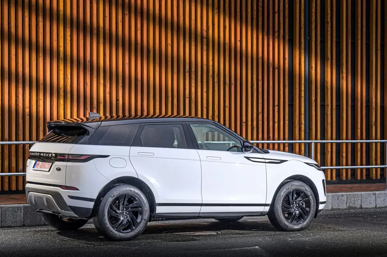 Weißer Range Rover Evoque Benziner mit schwarzem Dach parkt vor einer Holzwand.