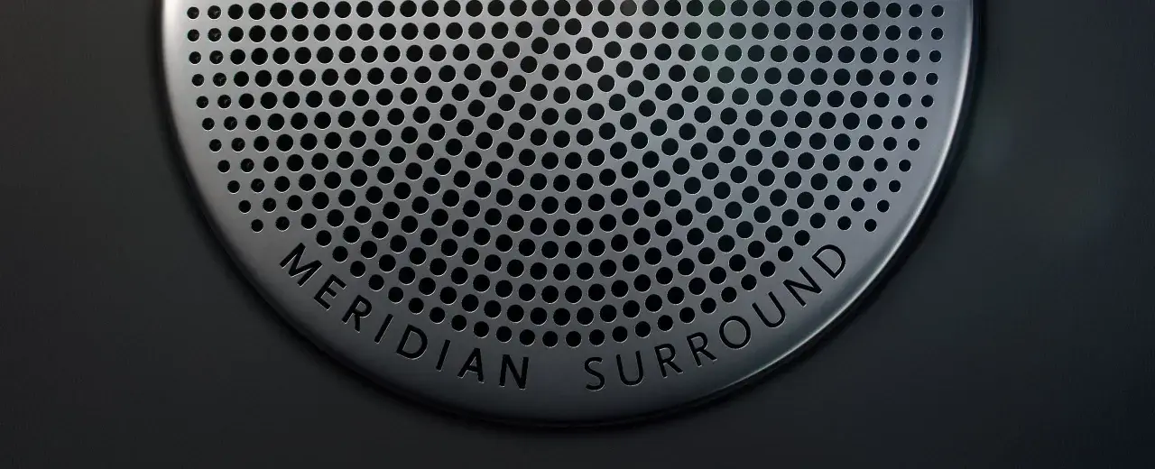 Nahaufnahme eines Lautsprechergitters mit der Aufschrift "MERIDIAN SURROUND". Gute Meridian Soundsystem Erfahrungen sind garantiert.