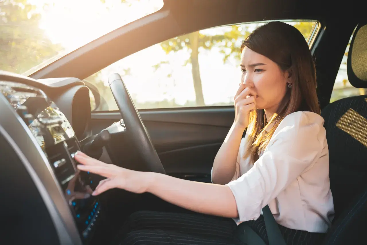 Frau hält sich die Nase zu, weil das Auto verbrannt riecht. Sie versucht, die Lüftung zu bedienen.