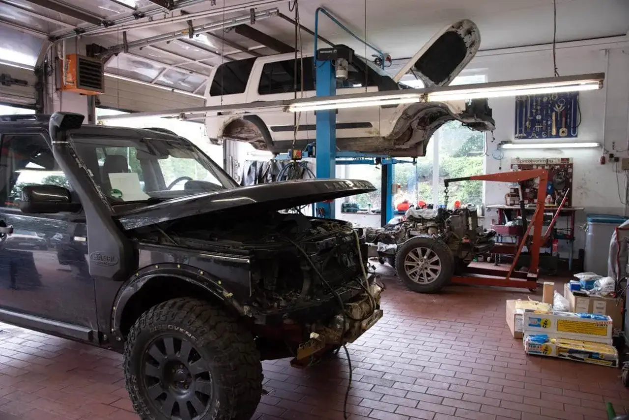 Werkstatt mit zwei Land Rover Discovery 4. Einer vorne mit geöffneter Haube, der andere auf der Hebebühne. Mögliche Schwachstellen werden hier behoben.