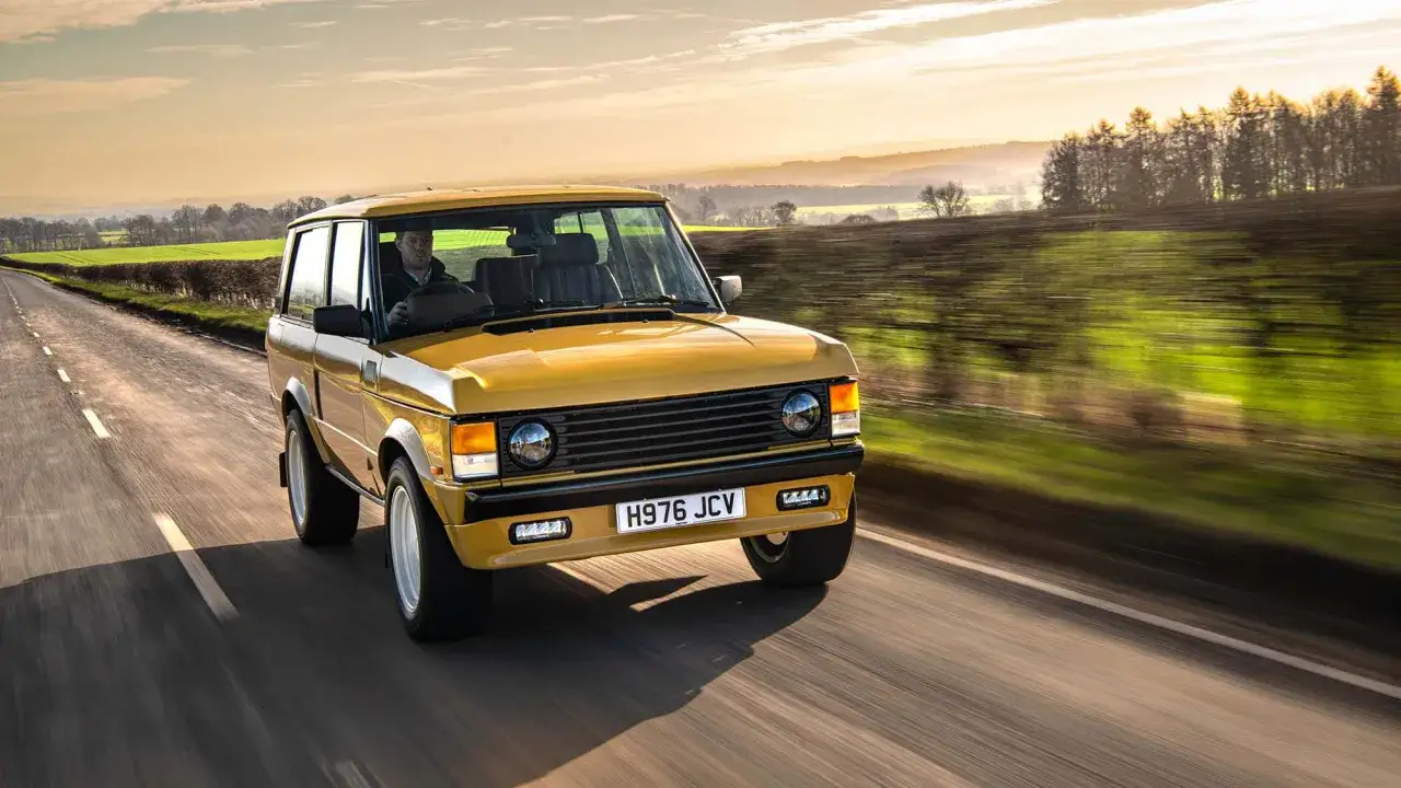 Gelber Range Rover 3-Türer fährt auf einer Landstraße bei Sonnenuntergang.