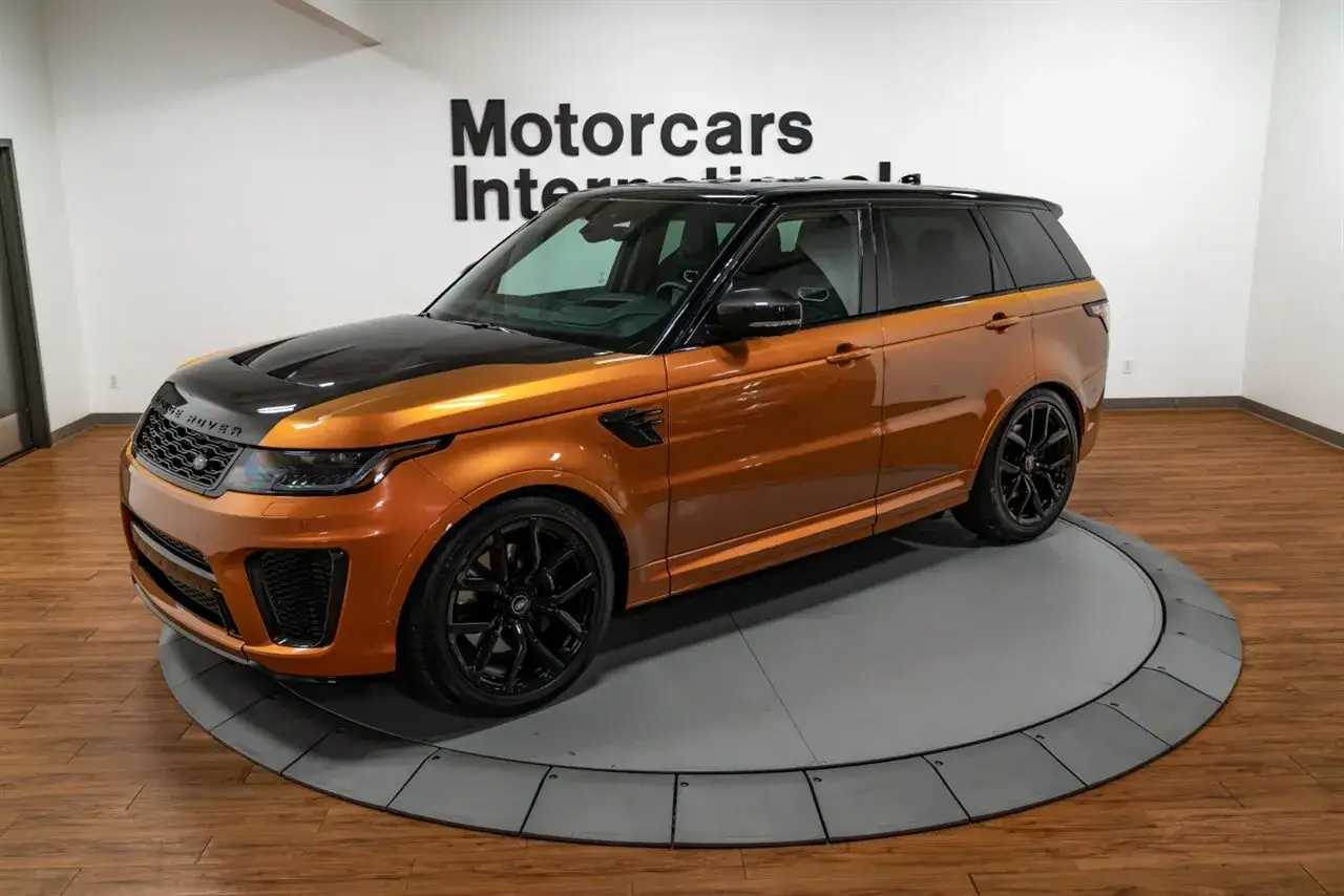 Ein leuchtend oranger Range Rover Sport mit schwarzer Motorhaube und Felgen steht auf einem Drehteller.