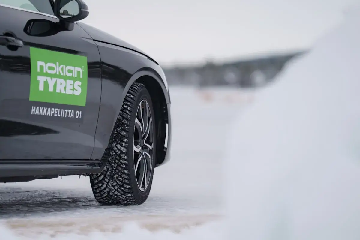 Schwarzes Auto mit Nokian Tyres Aufkleber und Spikes-Reifen auf verschneiter Straße. Reifen mit Spikes in Deutschland erlaubt für sichere Fahrt.