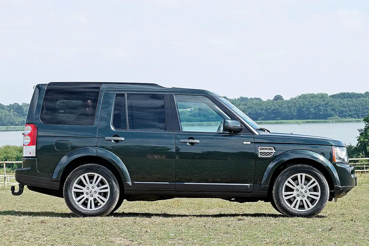 Dunkelgrüner Land Rover Discovery 4 im Profil, mit Blick auf die Landschaft. Bekannt für seine Geländetauglichkeit, aber auch für seine Land Rover Discovery 4 Schwachstellen.