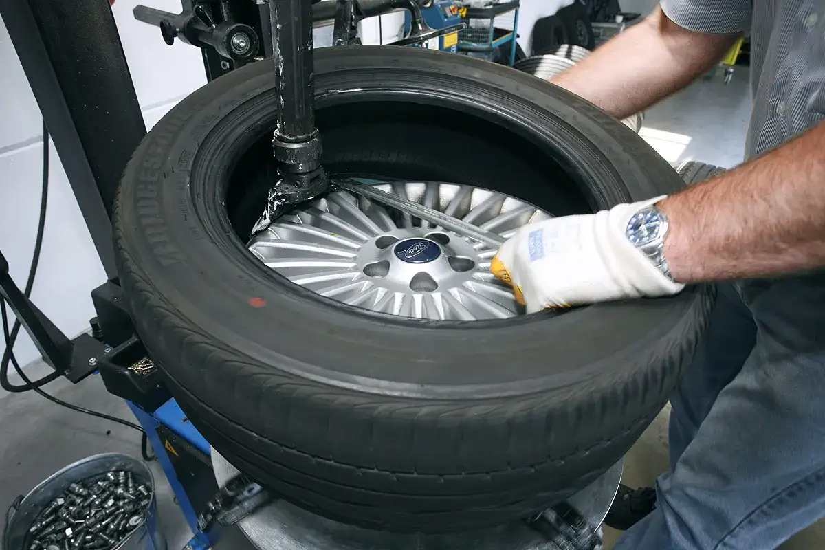 Ein Mechaniker wechselt einen Reifen auf einer Maschine. Er fragt sich, was kostet ein reifenwechsel?