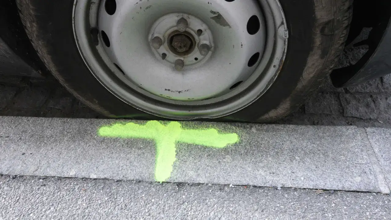 Ein Auto steht auf einem Bordstein, markiert mit grüner Farbe. Die Felge hat Kratzer, die Kosten für die Entfernung sind unklar.
