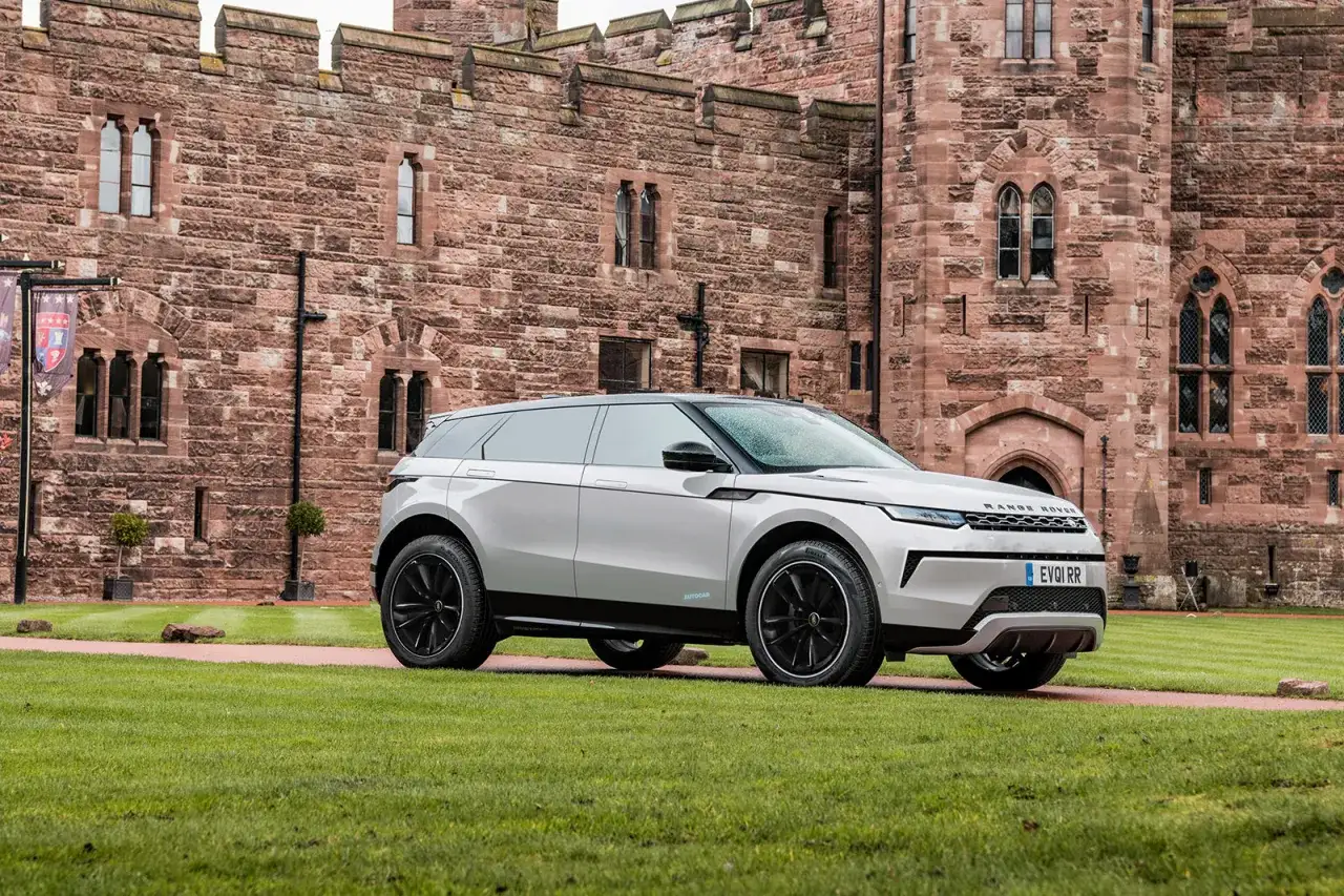 Ein kleiner Land Rover steht auf einem gepflegten Rasen vor einer imposanten Burg aus rotem Sandstein.