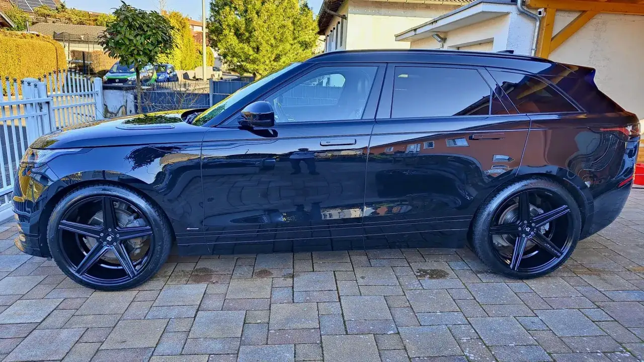 Schwarzer Range Rover Velar mit gl&auml;nzenden Alufelgen 22 Zoll, die im Sonnenlicht funkeln.