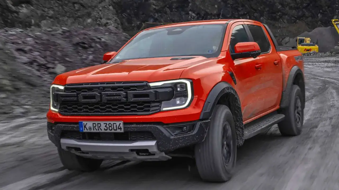 Orange Ford Ranger Raptor im Gel&auml;ndetest. Der Pickup meistert unwegsames Terrain, w&auml;hrend im Hintergrund ein Bagger zu sehen ist.