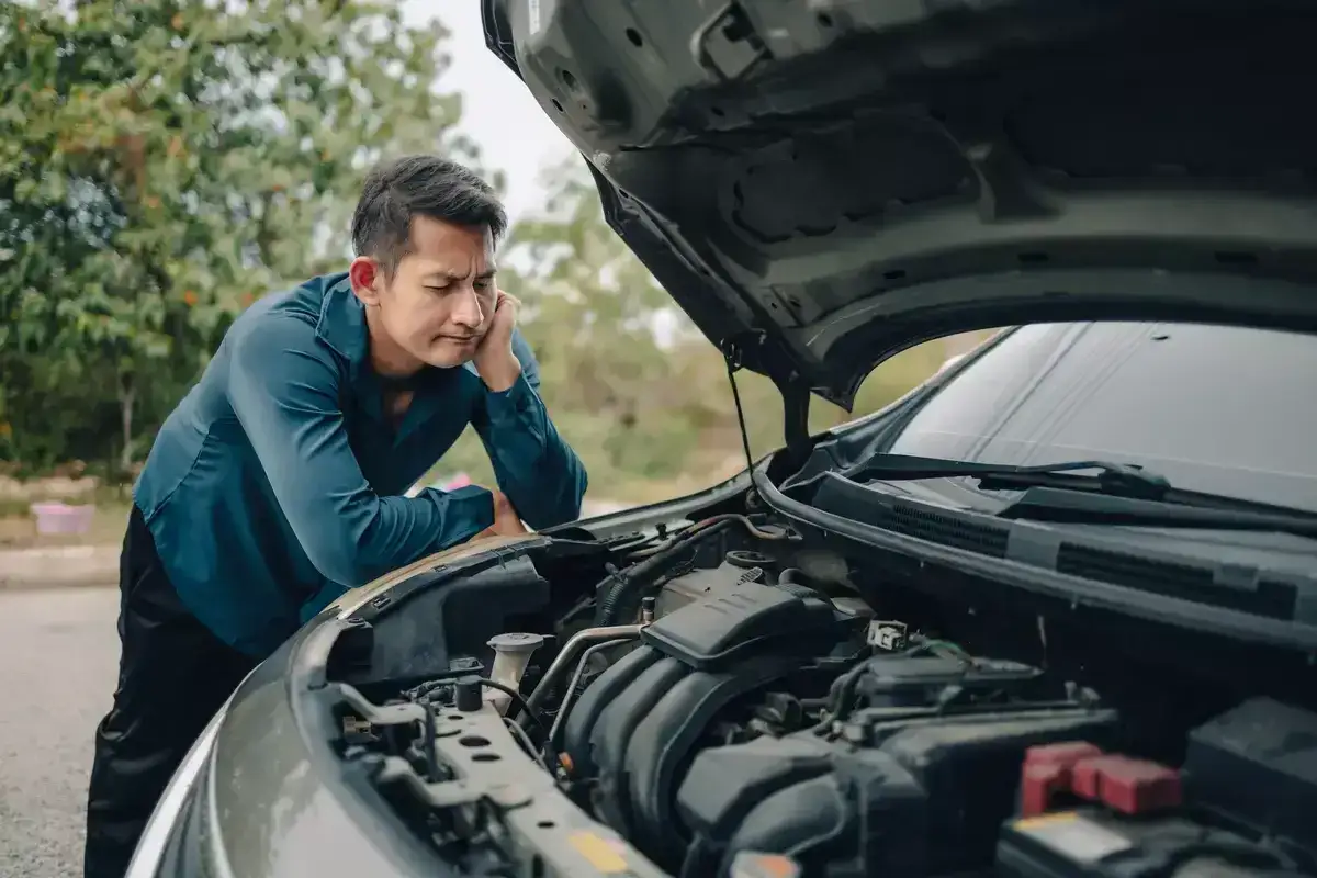 Besorgter Mann schaut in den offenen Motorraum. Sein Auto pfeift beim Fahren und er fragt sich, was los ist.