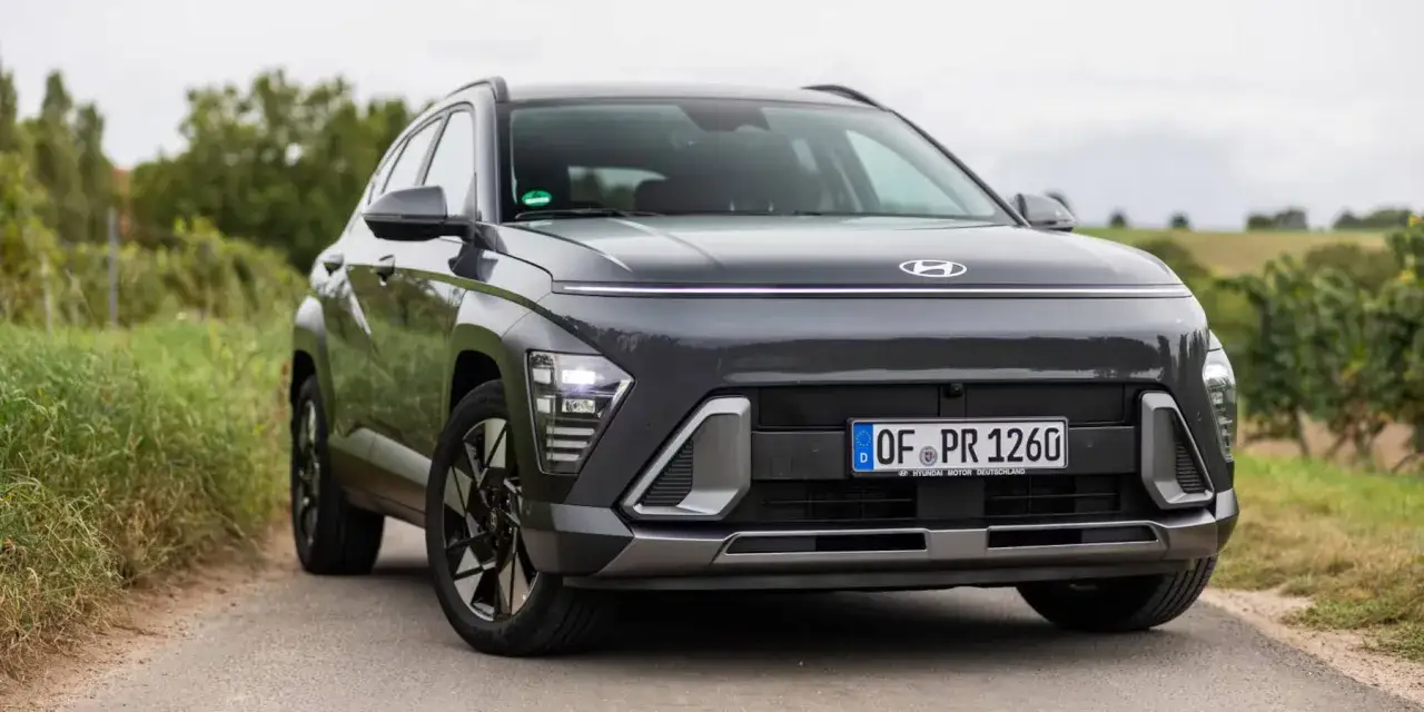 Der dunkle Hyundai Kona 2026 mit markanter Lichtleiste und LED-Scheinwerfern steht auf einer Landstraße, umgeben von grüner Natur.
