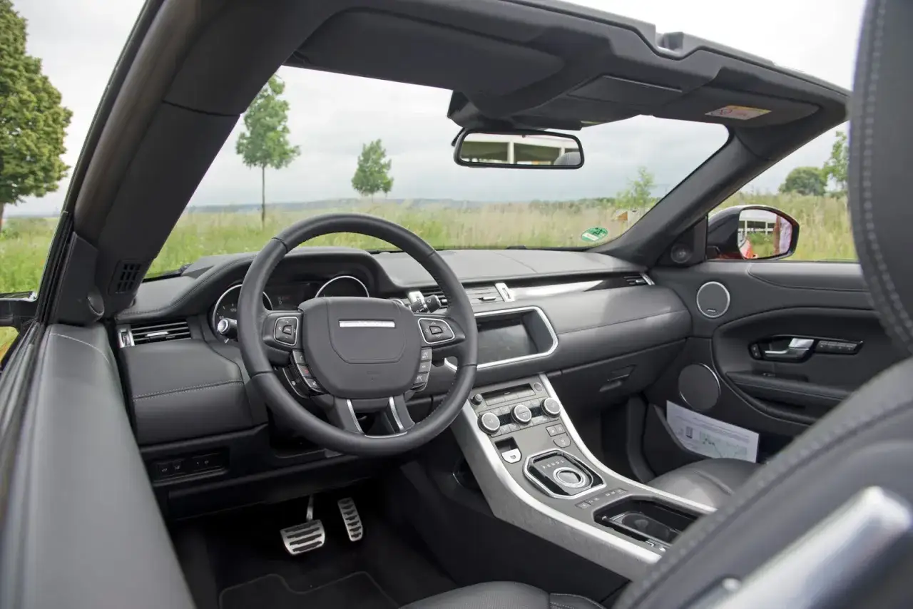 Interieur eines gebrauchten Evoque Cabrios mit Lederlenkrad, Mittelkonsole und Blick auf die offene Straße.