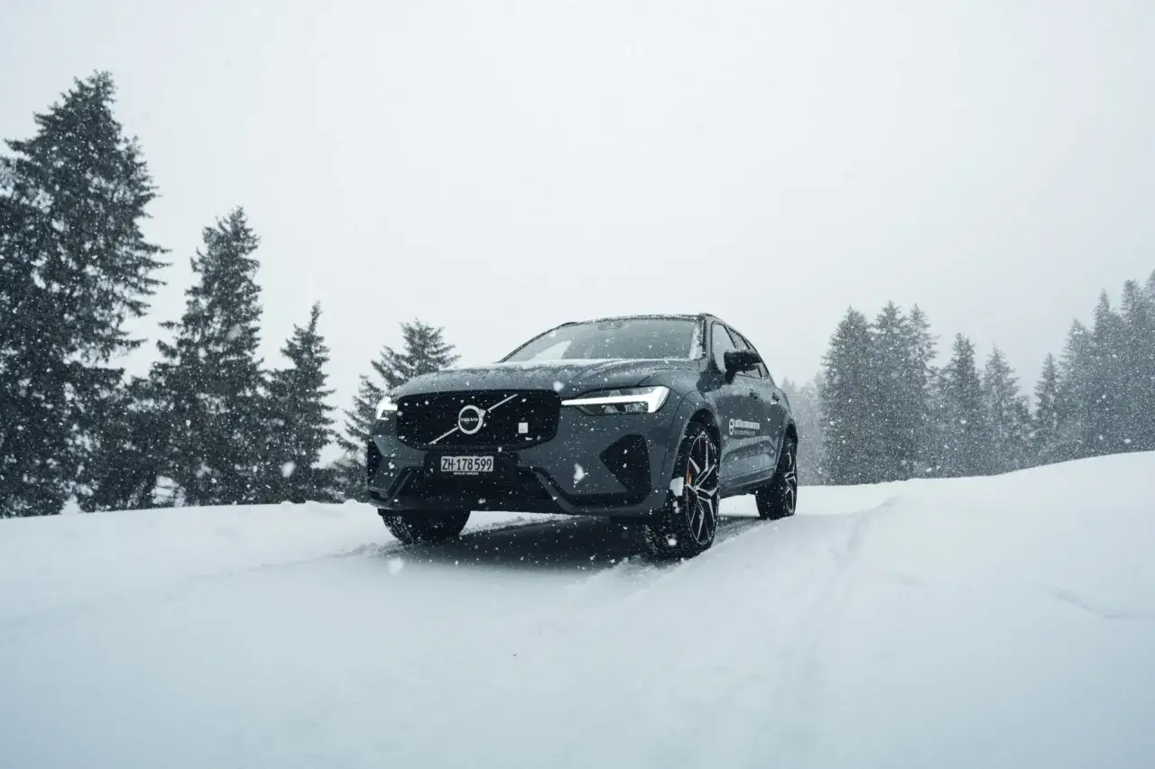 Dunkelgrauer Volvo f&auml;hrt durch verschneite Landschaft. Allrad-Schneeketten sorgen f&uuml;r Grip auf der eisigen Stra&szlig;e.