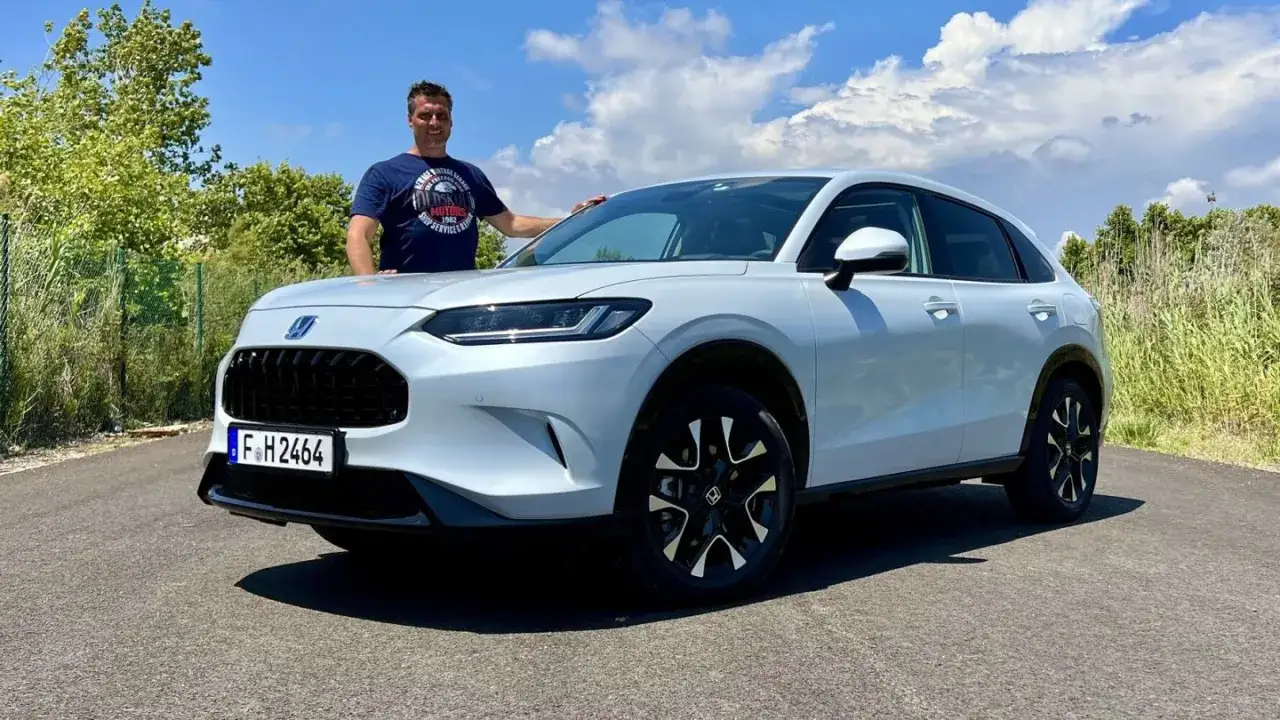 Mann neben wei&szlig;em Honda ZR-V mit schwarzem K&uuml;hlergrill und Felgen, sonniger Tag mit Wolken.