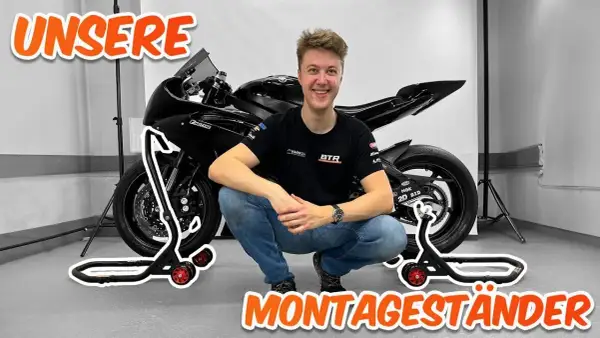 Ein Mann hockt neben einem Motorrad, das auf Montageständern steht. Perfekt, um das Motorrad hochzubocken!