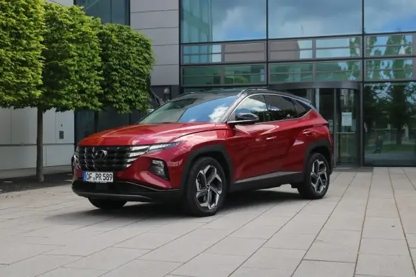 Roter Hyundai Tucson 2026 vor einem modernen Gebäude mit Bäumen.