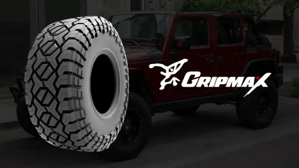 Ein grobstolliger Reifen von Gripmax neben einem roten Jeep. Perfekt für jedes Abenteuer.