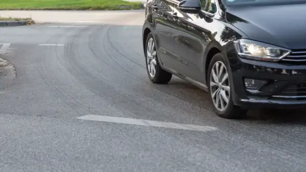 Schwarzes Auto fährt um eine Kurve, Reifen quietschen.