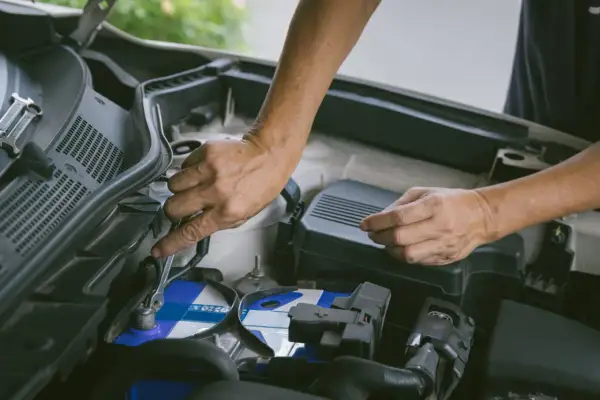 Hände wechseln eine Autobatterie. Ein Schraubenschlüssel löst die Klemmen. Start stop batterie wechseln ohne anlernen ist hier möglich.