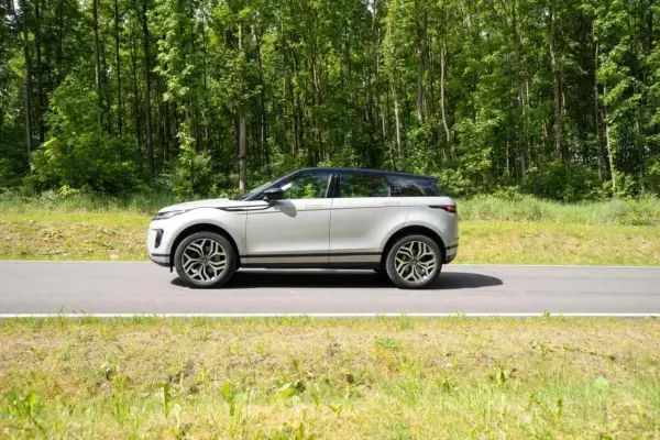 Ein silberner Range Rover Evoque fährt auf einer Straße durch einen grünen Wald.