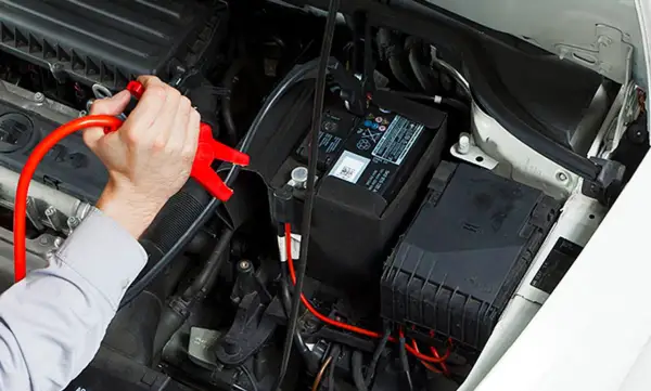 Hand hält rote Starthilfeklemme, die an der Autobatterie befestigt wird. Dies ist die zweite Batterie im Auto, die zum Starten benötigt wird.