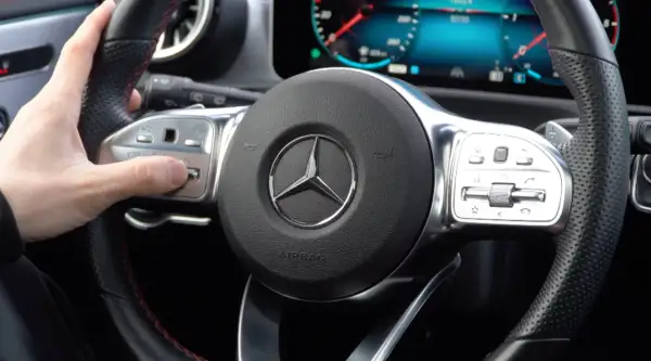 Hand stellt Mercedes Distronic ein. Lenkrad mit Bedienelementen und Stern-Logo.