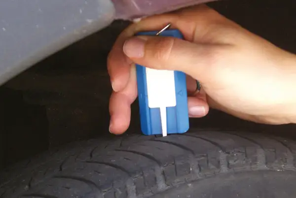 Hand misst Profiltiefe eines Reifens mit einem Messgerät. So prüfen Sie, wie alt Winterreifen sind.