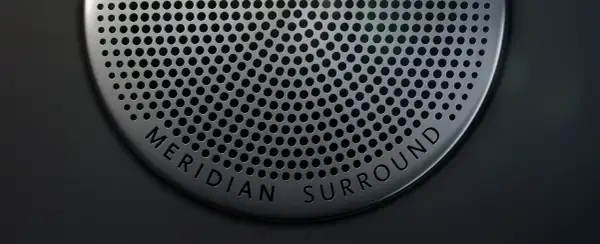 Nahaufnahme eines Lautsprechergitters mit der Aufschrift "MERIDIAN SURROUND". Gute Meridian Soundsystem Erfahrungen sind garantiert.